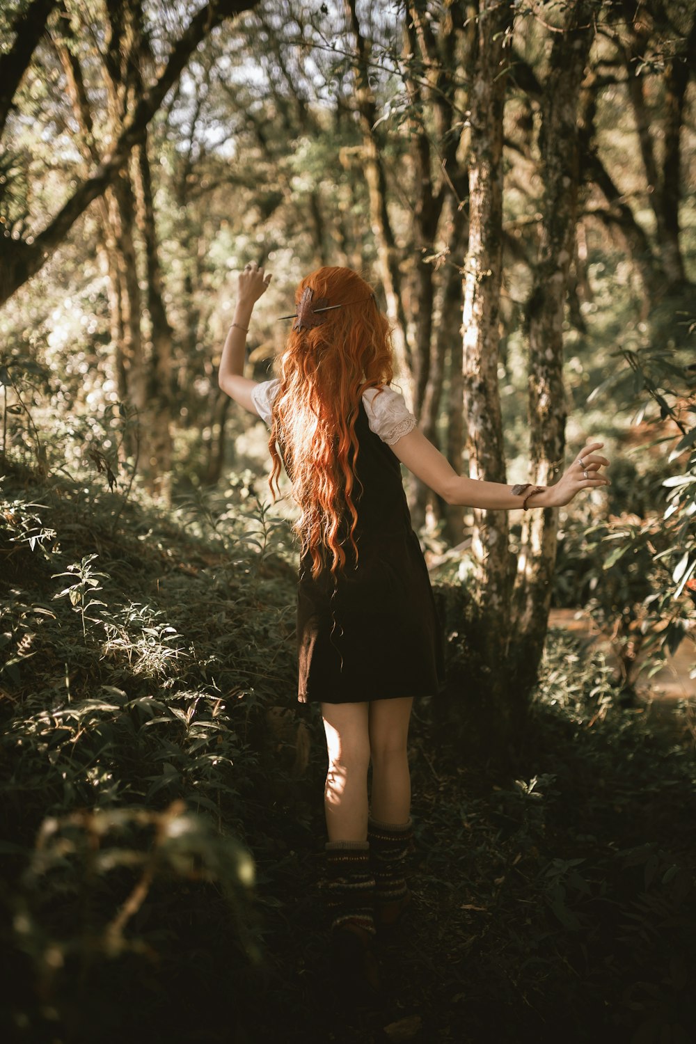 a woman with long red hair walking through a forest