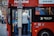A person is stepping off a red double-decker bus with the destination sign '31 White City Bus Station.' There is a sign indicating it's an alighting point only. The bus is parked on a city street with buildings in the background.
