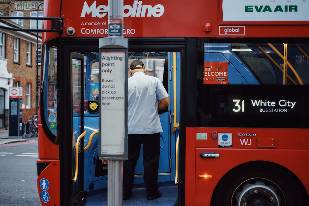 a man getting on a red bus at a bus stop