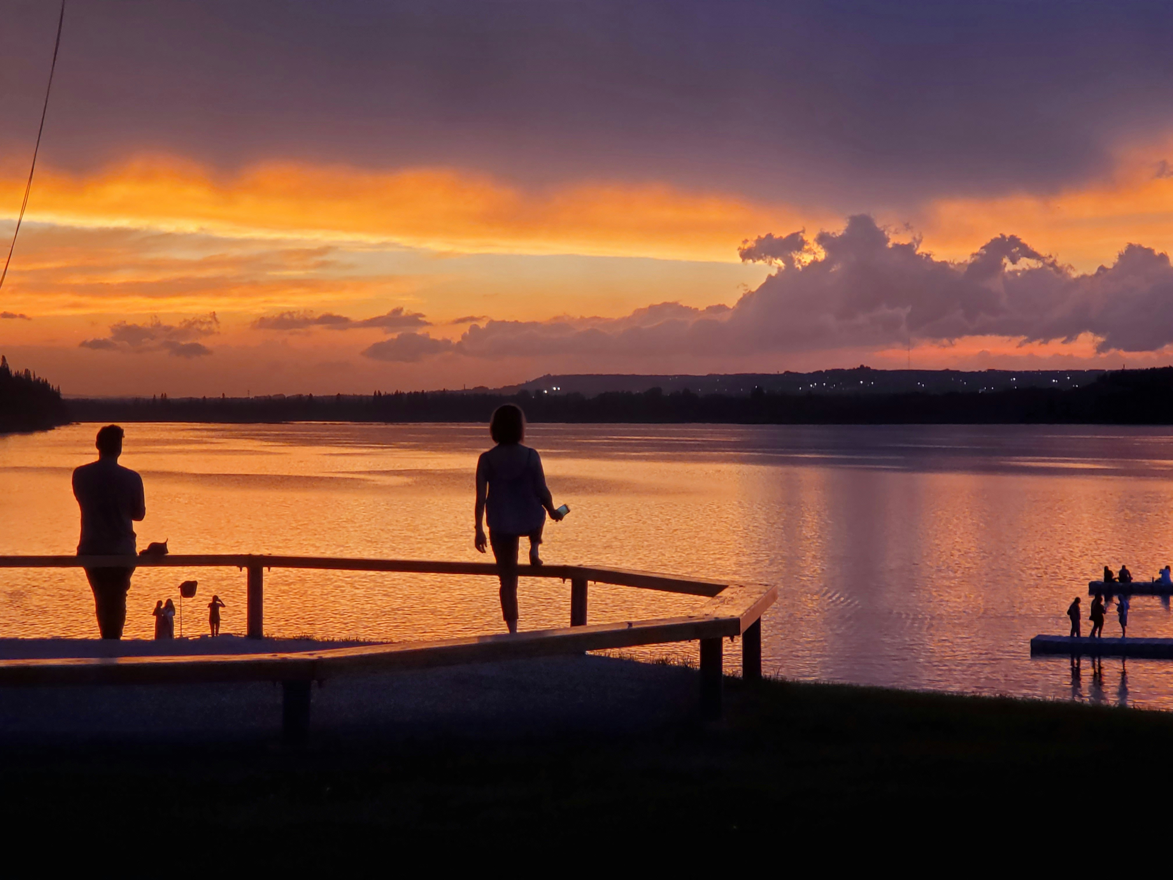 Dos personas de pie en un muelle mirando la puesta de sol