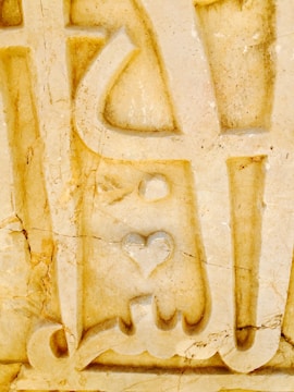 An intricate stone carving featuring abstract shapes and a prominent heart symbol. The surface is textured with visible cracks and variations in color, adding a rustic and weathered appearance.