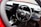 The interior of a car showcasing a steering wheel with the Honda logo prominently displayed. The dashboard is modern with digital screens and various control buttons. The surrounding area includes a gear shift and other car controls, suggesting a high-tech, contemporary vehicle interior.