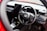 The interior of a car showcasing a steering wheel with the Honda logo prominently displayed. The dashboard is modern with digital screens and various control buttons. The surrounding area includes a gear shift and other car controls, suggesting a high-tech, contemporary vehicle interior.