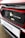 The image features a close-up of an electric car's charging port, with the Honda logo visible. The car is predominantly red with black and white accents. A sign with the text 'Swansway Motor Group' is prominently displayed below the charging area.