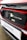 The image features a close-up of an electric car's charging port, with the Honda logo visible. The car is predominantly red with black and white accents. A sign with the text 'Swansway Motor Group' is prominently displayed below the charging area.