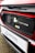 The image features a close-up of an electric car's charging port, with the Honda logo visible. The car is predominantly red with black and white accents. A sign with the text 'Swansway Motor Group' is prominently displayed below the charging area.