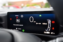 A close-up view of a car's digital dashboard displaying various indicators such as speed, gear position, and mileage. The central panel shows a speed of 0 mph with the gear set to Park. Additional information includes battery charge at 87%, a remaining range of 163 miles, and a prompt to press a switch to operate. The display is primarily black with white, red, and green icons and text.
