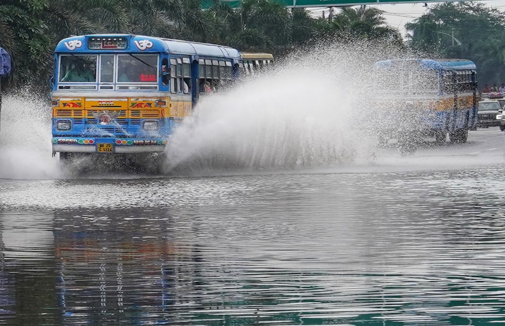 a blue and yellow bus driving down a flooded street