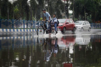 a couple of men riding bikes through a flooded street