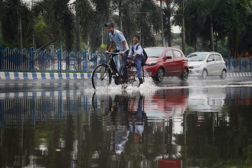 a couple of men riding bikes through a flooded street