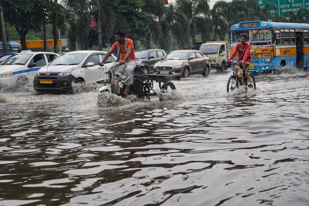 a couple of people riding bikes through a flooded street