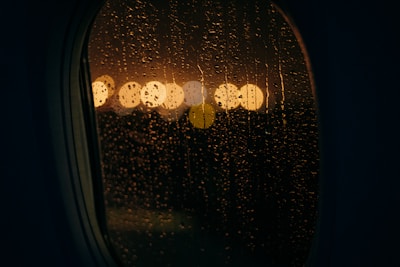 City lights sparkling below a night flight, seen through a rain-speckled airplane window.