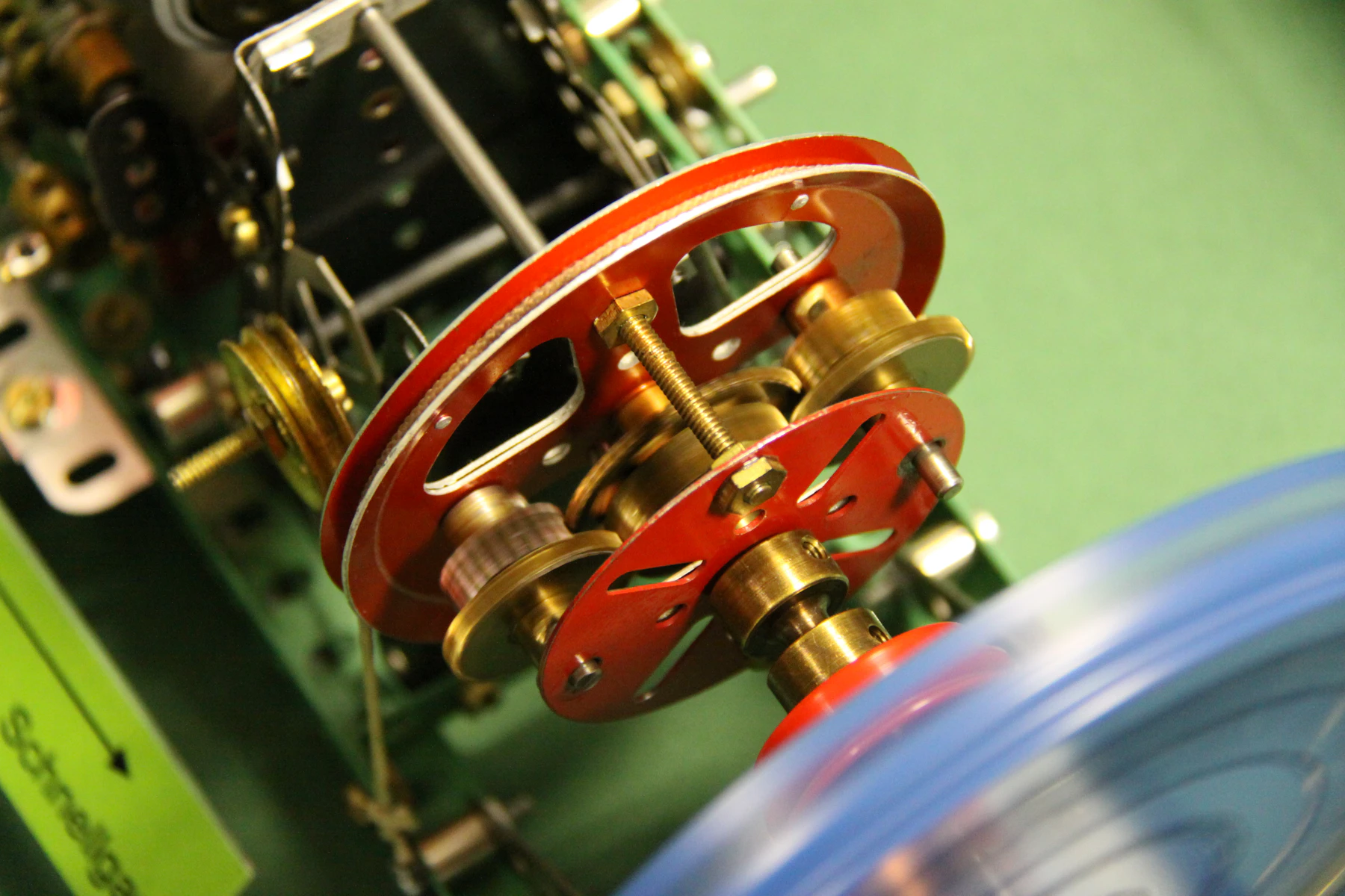 Close-up of red spoked wheels and brass gears on a shaft inside a metal-strip mechanism