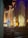 A dimly lit church interior with tall, ornate columns and stained glass windows. Decorations include a brightly lit Christmas tree adorned with blue and white lights, surrounded by festive garlands and wreaths. Empty pews lead to the altar, which is bathed in a warm orange glow.