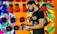 A man standing in front of a colorful wall holds a pair of black boxing gloves. The wall features vibrant painted patterns and is lined with red and blue boxing gloves.