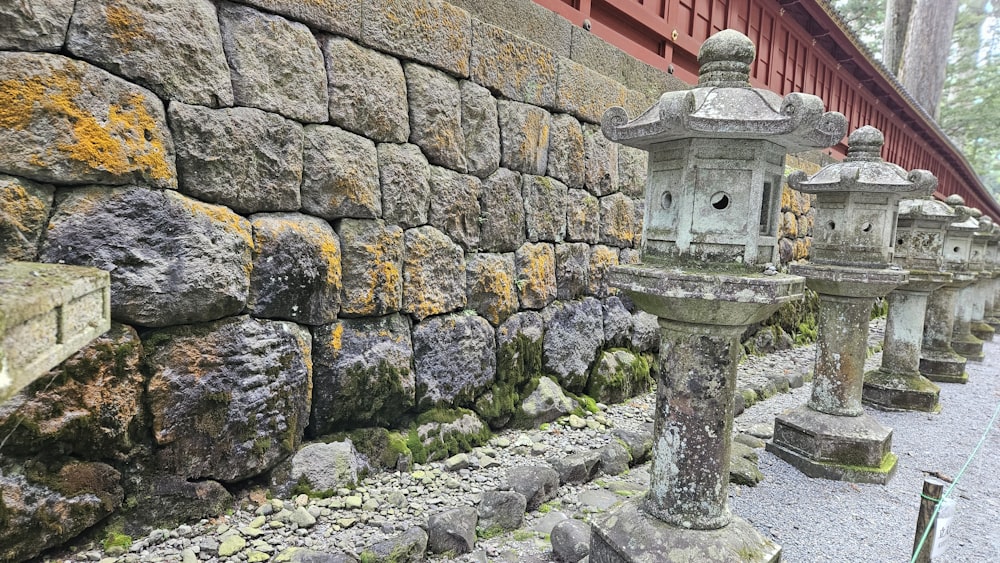 eine Reihe steinerner Laternen, die neben einer Steinmauer sitzen