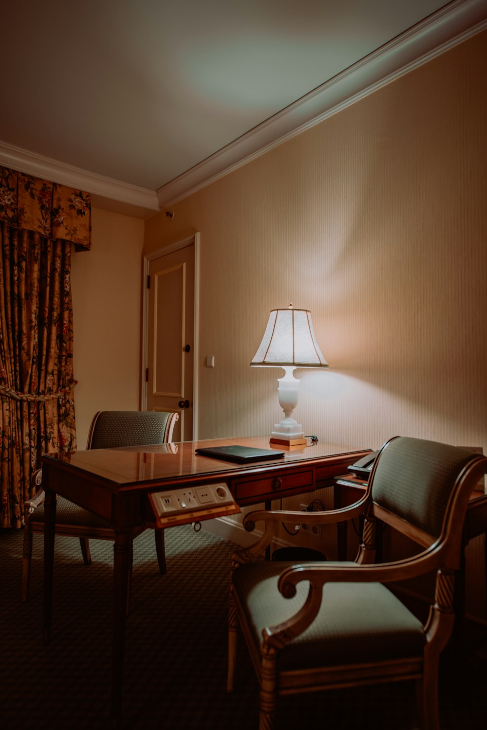 a hotel room with a desk, chair and lamp