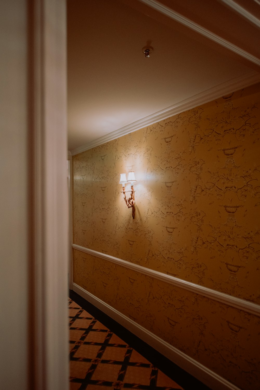 a hallway with a lamp on the wall and a checkered floor