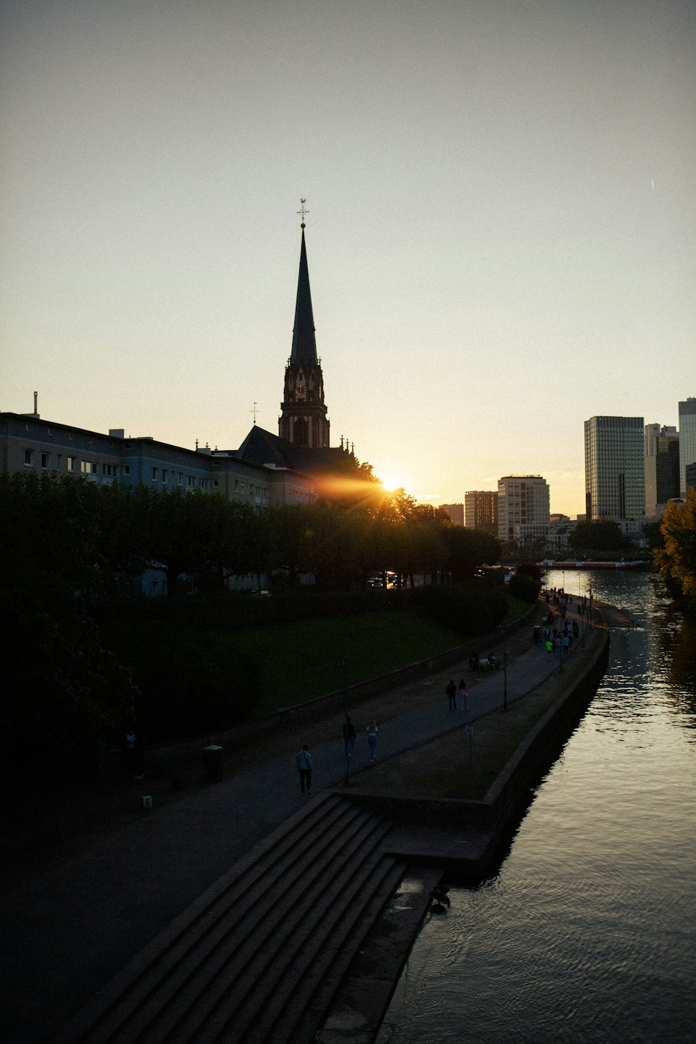 the sun is setting over a river with a church steeple in the background