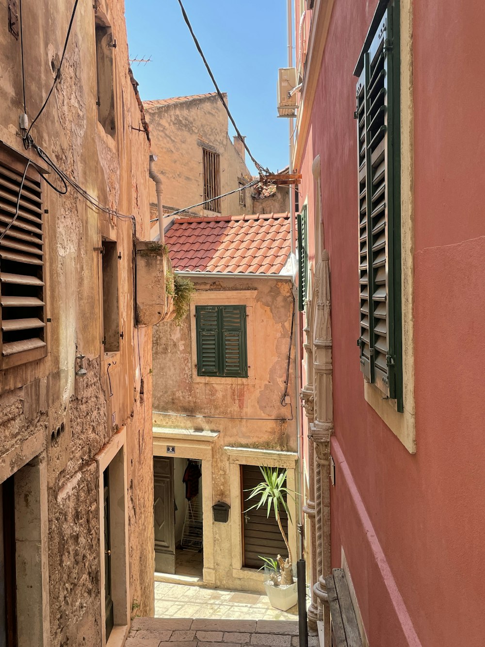 a narrow alleyway between two buildings with shutters open