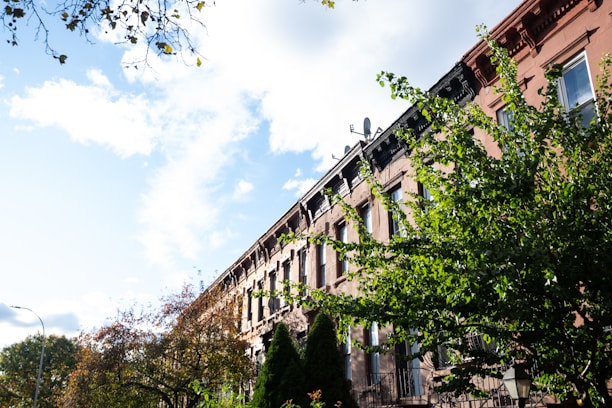 Modern brownstone exterior with lush trees lining a quiet New York City street.
