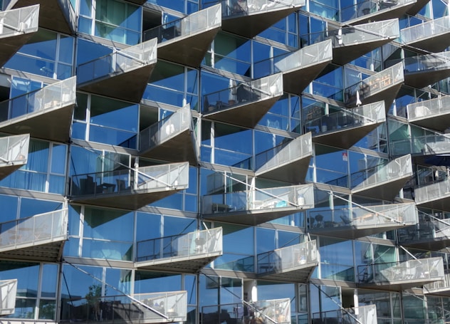 A series of modern, angular balconies protruding from a building with reflective glass windows. The balconies are arranged in a repeating geometric pattern, creating a dynamic architectural facade.