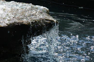 Close-up of water rushing over the edge, droplets sparkling in the sunlight.