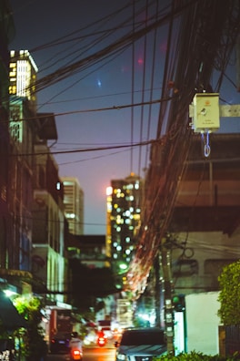 Evening scene showing illuminated cityscape with visible cable lines connecting buildings.