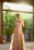 Elegant woman wearing a soft pink Lumina Atelier dress in a sunlit boutique.