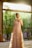 A stylish woman wearing elegant linen clothing, standing in a sunlit room with soft textures and neutral colors.