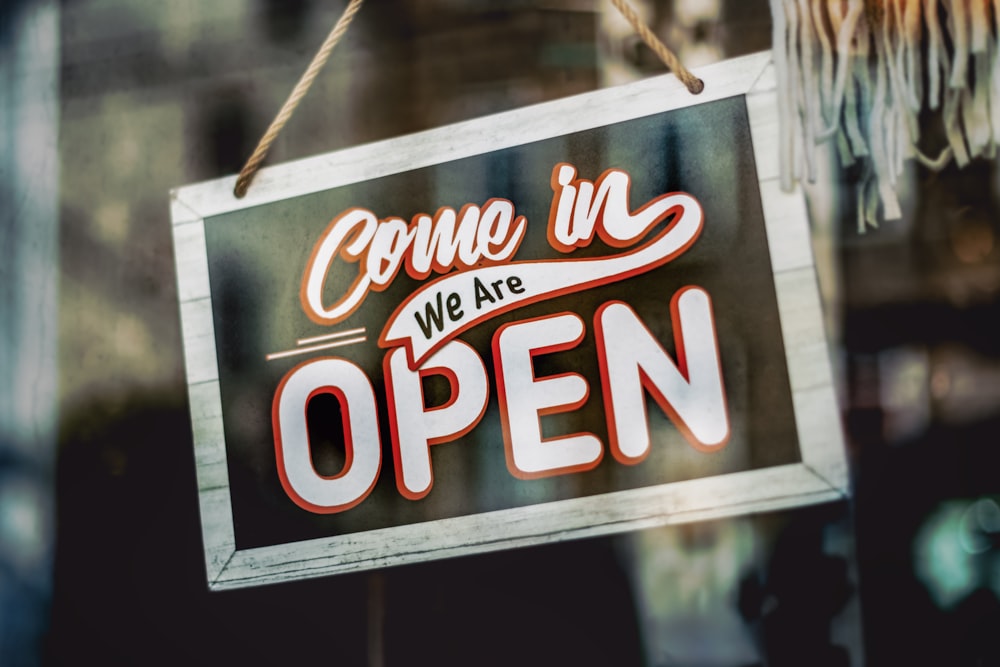 a sign hanging from a glass window that says come in we are open