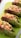 Several green tea-flavored bread rolls are filled with a mixture of scrambled eggs or tofu, diced cucumbers, and chopped red bell peppers. The rolls are arranged neatly on a bright green cutting board with a perforated white surface visible on the side.