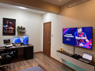 A happy gamer browsing affordable game deals on a laptop in a cozy room filled with gaming gear.