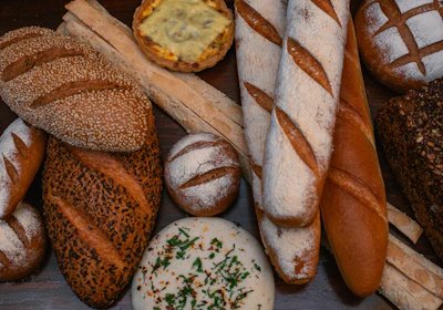 An assortment of breads including seeded loaves, baguettes, and rustic rolls artfully arranged on a linen cloth.