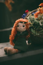 A colorful crochet doll sitting next to a wooden framed artwork on a shelf.