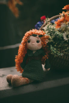 A colorful crochet doll sitting next to a wooden framed artwork on a shelf.