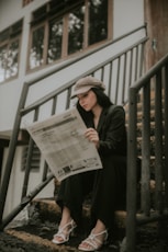 a woman sitting on the steps reading a newspaper