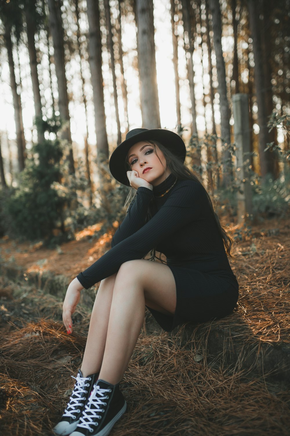 a woman in a black dress and hat sitting on the ground