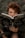 A person with curly hair is intensely looking over an open book titled 'Bruxa Natural,' amidst a lush green background, creating a mysterious and earthy atmosphere.