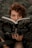 A person with curly hair is intensely looking over an open book titled 'Bruxa Natural,' amidst a lush green background, creating a mysterious and earthy atmosphere.