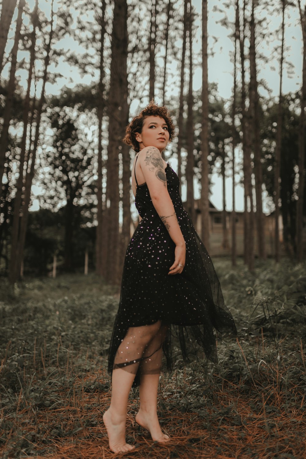 a woman in a black dress standing in a forest