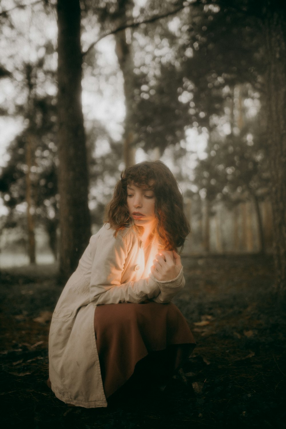 a woman sitting in the woods holding a lit candle