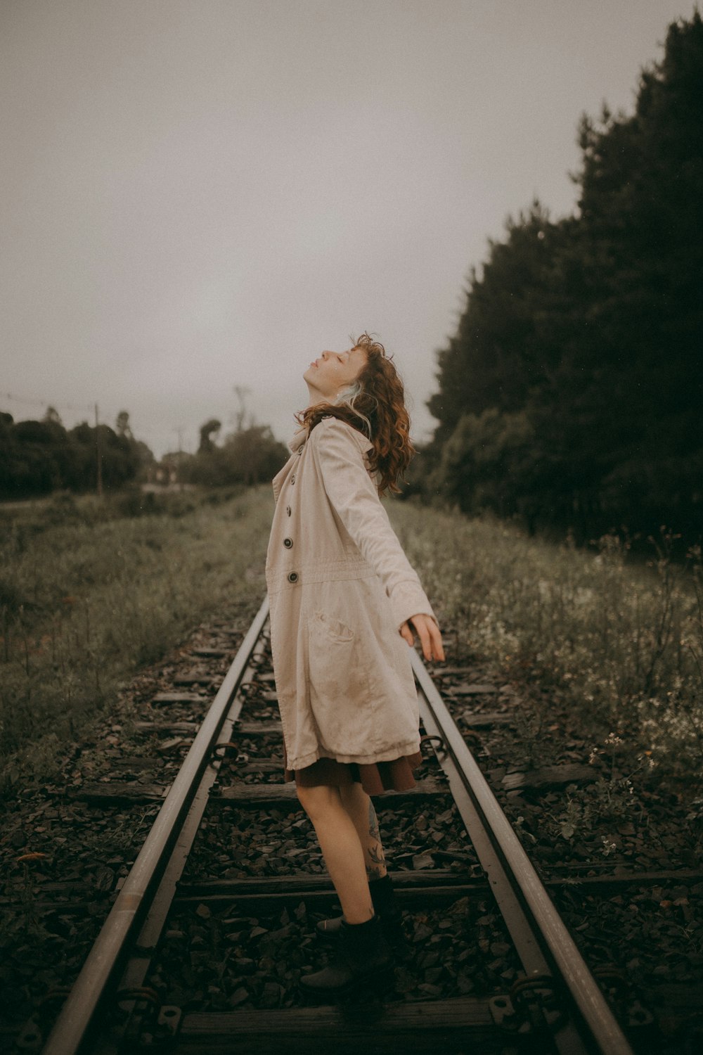 a woman in a trench coat walking on a train track