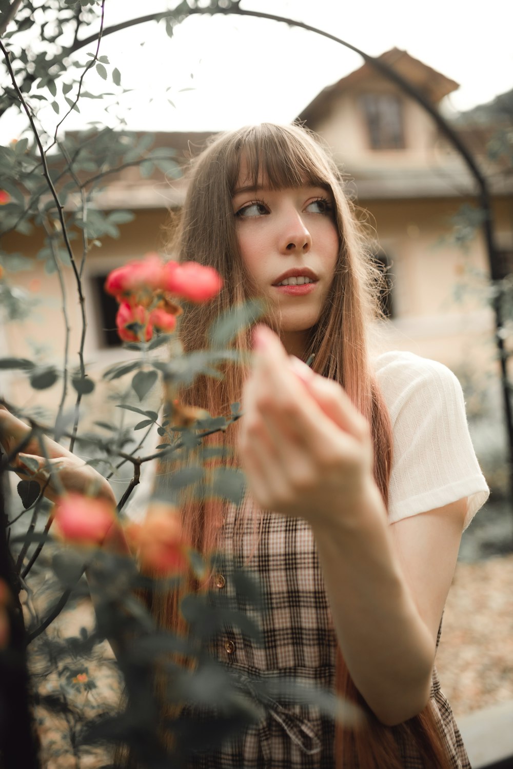 a woman with long hair standing next to a bush