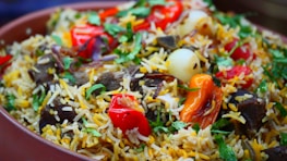 A vibrant dish filled with long-grain rice, herbs, and spices. The rice is garnished with fresh cilantro, red and yellow bell peppers, onions, and pieces of meat, creating a colorful and appetizing presentation.