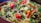 A vibrant dish filled with long-grain rice, herbs, and spices. The rice is garnished with fresh cilantro, red and yellow bell peppers, onions, and pieces of meat, creating a colorful and appetizing presentation.
