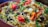 A vibrant dish filled with long-grain rice, herbs, and spices. The rice is garnished with fresh cilantro, red and yellow bell peppers, onions, and pieces of meat, creating a colorful and appetizing presentation.