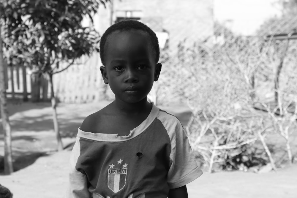 a young boy standing in front of a tree