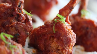 Close-up view of crispy, fried pieces of chicken with a rich, reddish-brown coating, garnished with fresh green herbs.