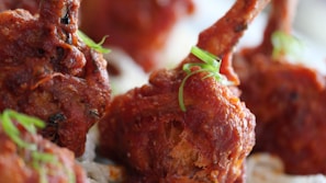 Close-up view of crispy, fried pieces of chicken with a rich, reddish-brown coating, garnished with fresh green herbs.